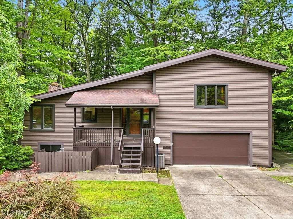 Tri-level home featuring an attached garage, stairs, concrete driveway, a porch, and view of wooded area