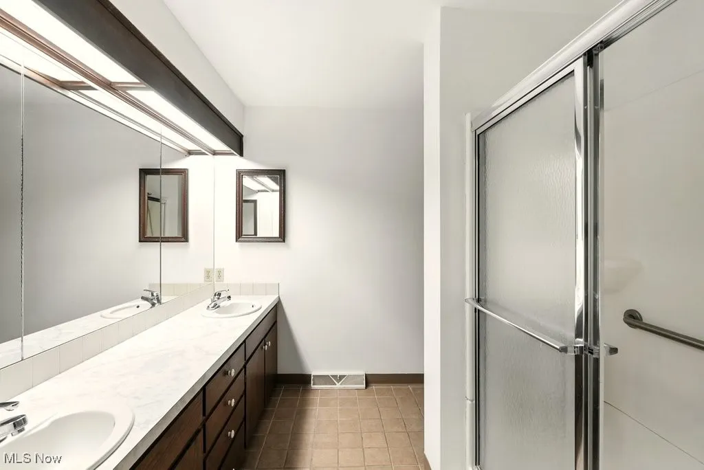 Bathroom with double vanity, a shower stall, and light tile patterned floors