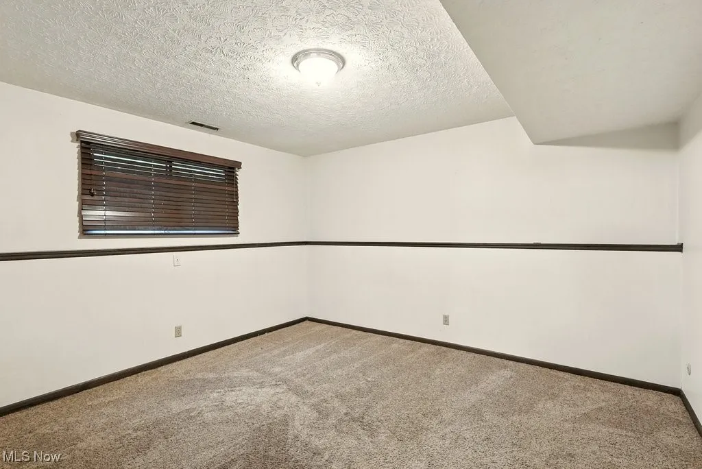 Empty room with light colored carpet and a textured ceiling