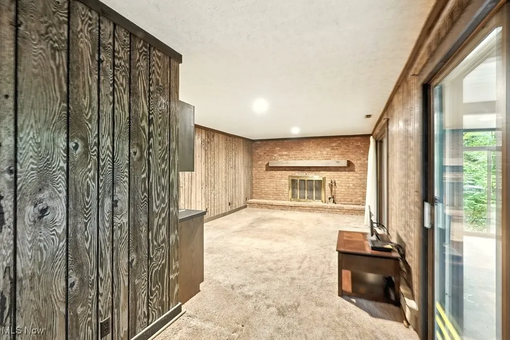 Unfurnished living room with a brick fireplace, light carpet, wood walls, ornamental molding, and a textured ceiling