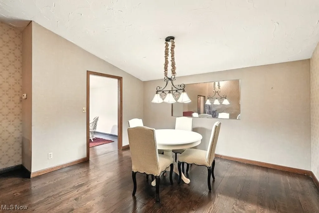 Dining area featuring dark wood-style flooring, vaulted ceiling, and wallpapered walls