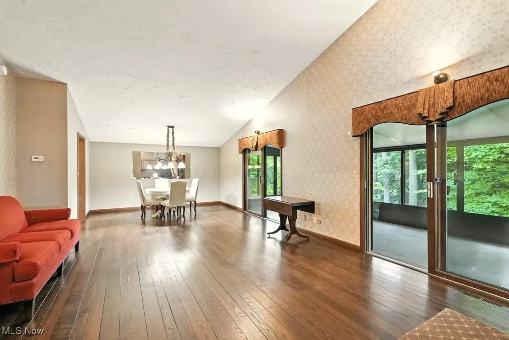 Living area with dark wood-style floors, plenty of natural light, vaulted ceiling, wallpapered walls, and a textured ceiling