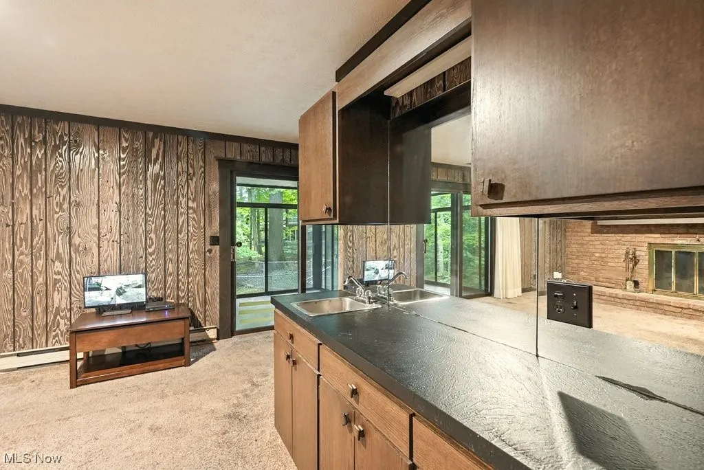 Kitchen featuring wood walls, light colored carpet, dark countertops, baseboard heating, and brown cabinetry