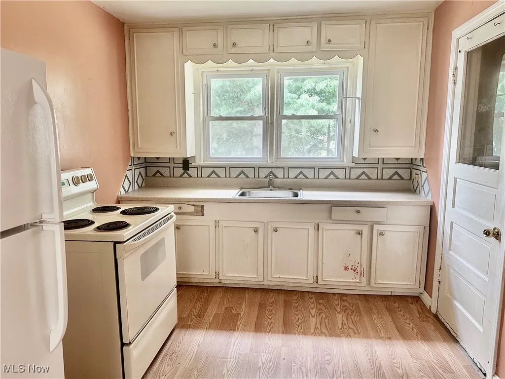 Kitchen with white appliances, light countertops, light wood-style flooring, and decorative backsplash