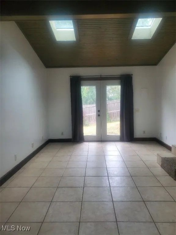 Spare room with a skylight, french doors, light tile patterned flooring, and vaulted ceiling