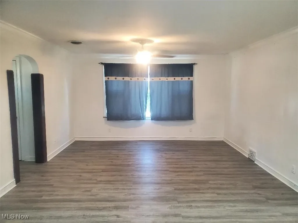 Empty room with dark wood-type flooring, arched walkways, and a ceiling fan