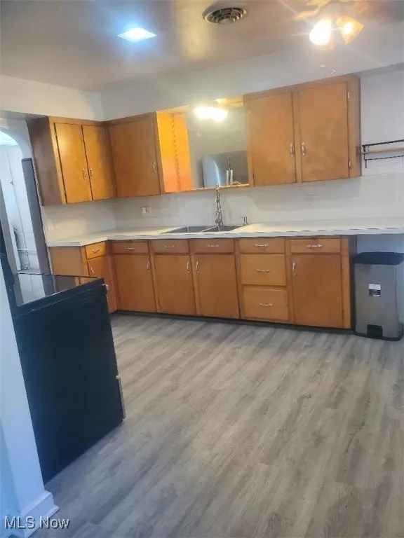 Kitchen with light countertops, brown cabinets, light wood-style flooring, decorative backsplash, and arched walkways