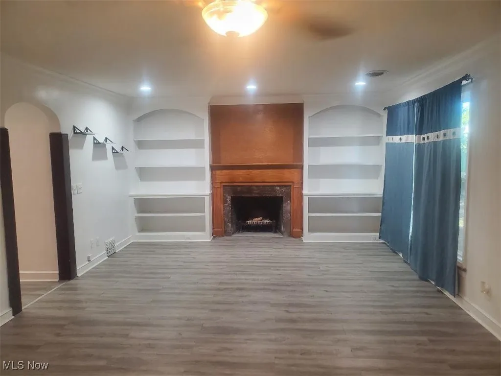 Unfurnished living room with built in shelves, a premium fireplace, and light wood-type flooring