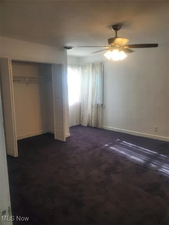 Unfurnished bedroom featuring dark carpet, a ceiling fan, and a closet