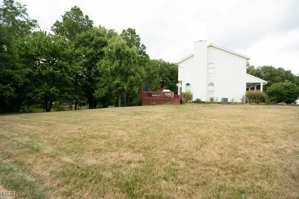 View of grassy yard with a deck and view of scattered trees