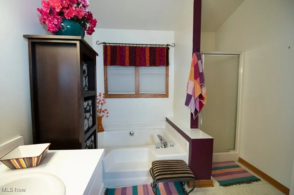 Full bath featuring vanity, a bath, a stall shower, and light tile patterned floors