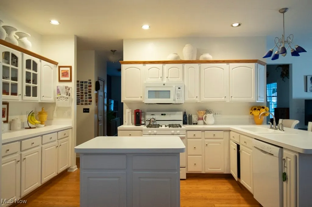 Kitchen featuring light countertops, light wood-style flooring, white appliances, a center island, and recessed lighting