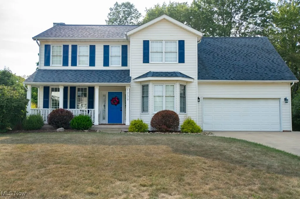 Traditional home with a porch, concrete driveway, a front yard, a garage, and a shingled roof