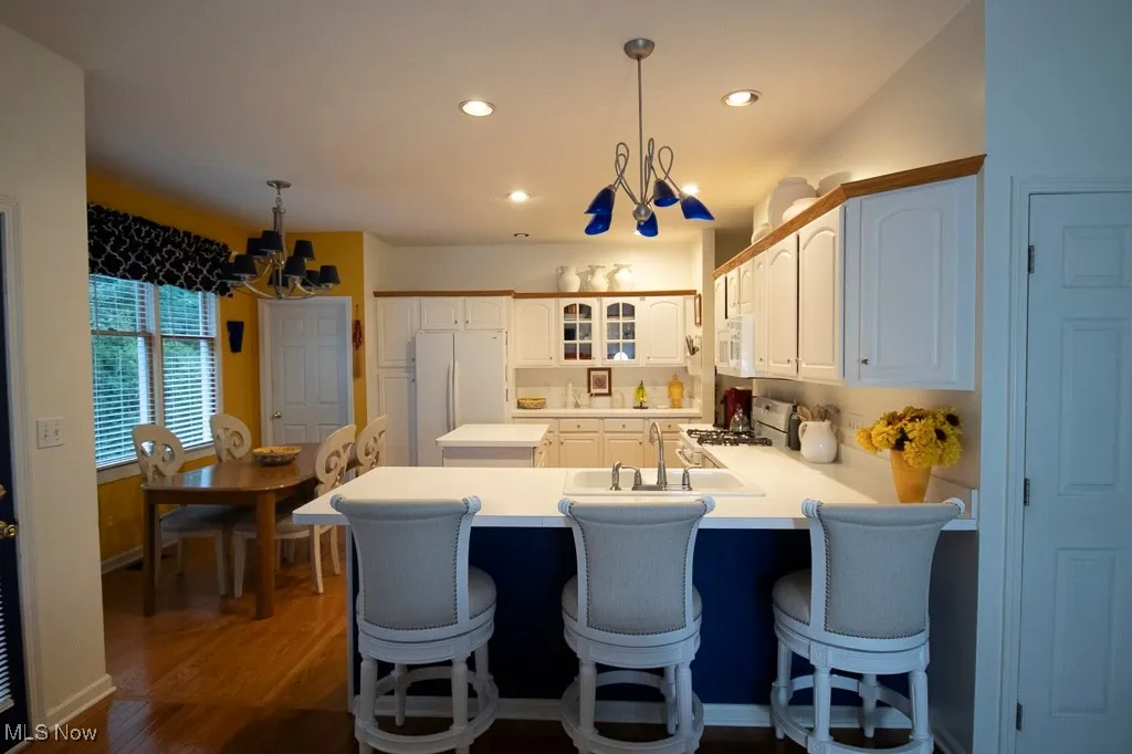 Kitchen featuring hanging light fixtures, a chandelier, light countertops, a breakfast bar area, and glass insert cabinets