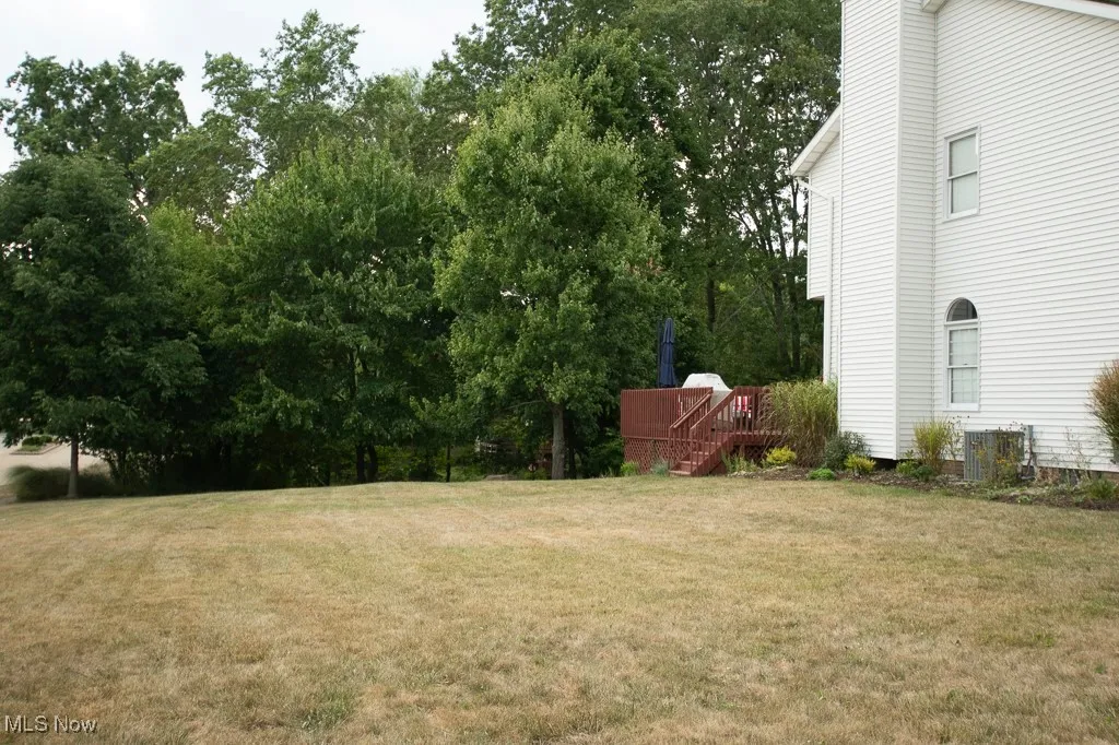 View of grassy yard featuring a deck and view of scattered trees