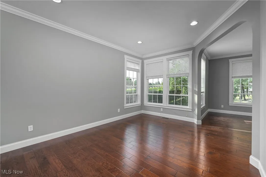 Spare room with crown molding, dark wood-type flooring, recessed lighting, and arched walkways