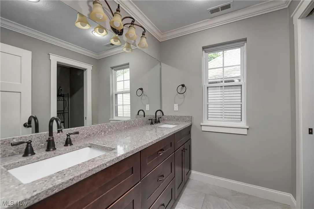 Bathroom with plenty of natural light, crown molding, double vanity, and a chandelier