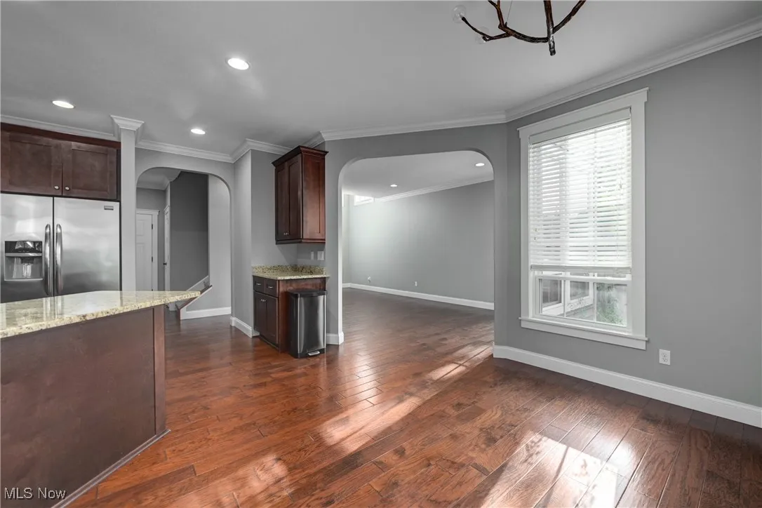 Kitchen featuring stainless steel fridge with ice dispenser, recessed lighting, crown molding, light stone counters, and dark brown cabinetry