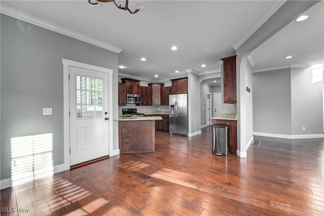 Kitchen featuring dark wood-style floors, stainless steel appliances, dark brown cabinets, open floor plan, and arched walkways