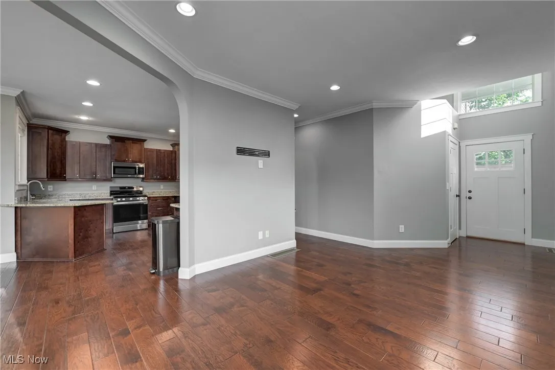 Unfurnished living room with dark wood-style floors, arched walkways, recessed lighting, and ornamental molding