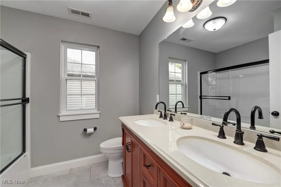 Full bathroom featuring double vanity, enclosed tub / shower combo, and light tile patterned floors