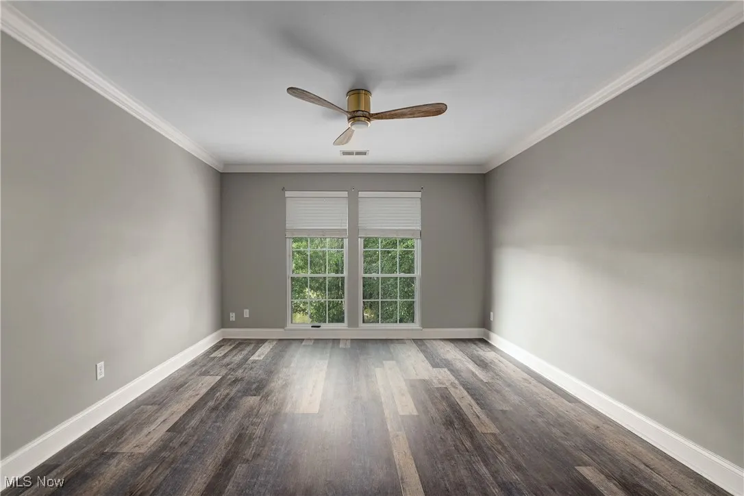 Unfurnished room featuring ornamental molding, dark wood-type flooring, and a ceiling fan