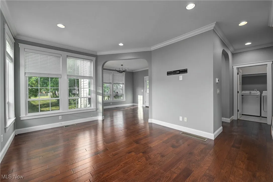 Unfurnished living room with arched walkways, crown molding, a chandelier, recessed lighting, and dark wood-style floors