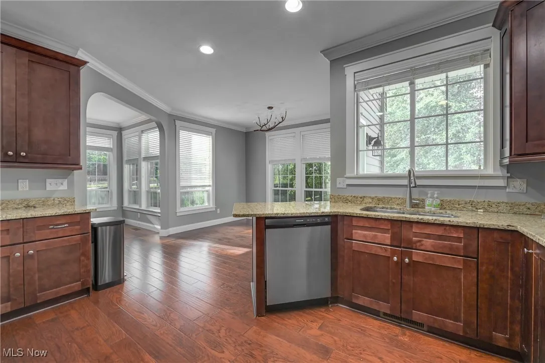 Kitchen with crown molding, light stone counters, stainless steel dishwasher, a peninsula, and arched walkways