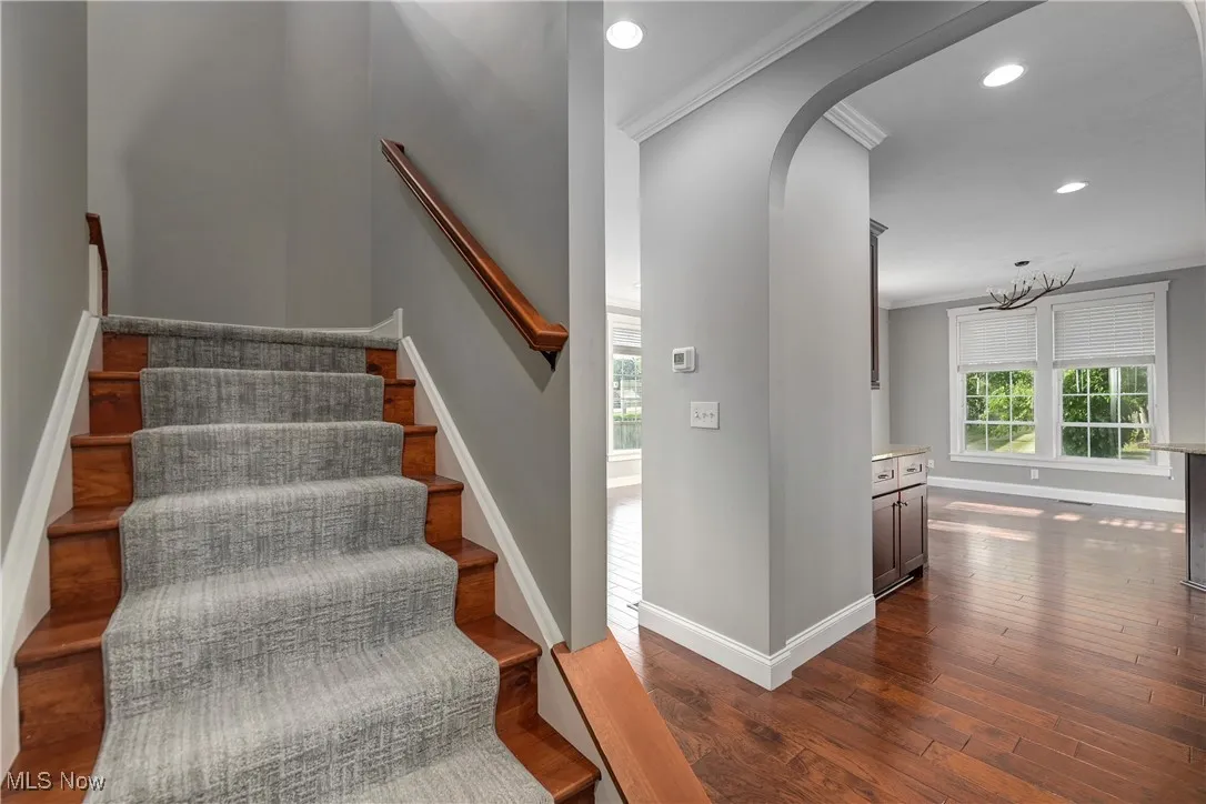 Stairway with crown molding, hardwood / wood-style flooring, recessed lighting, arched walkways, and a chandelier