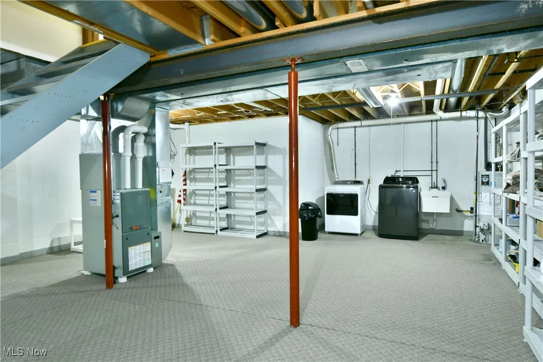 Unfinished basement featuring heating unit, carpet flooring, washing machine and dryer, and concrete block wall