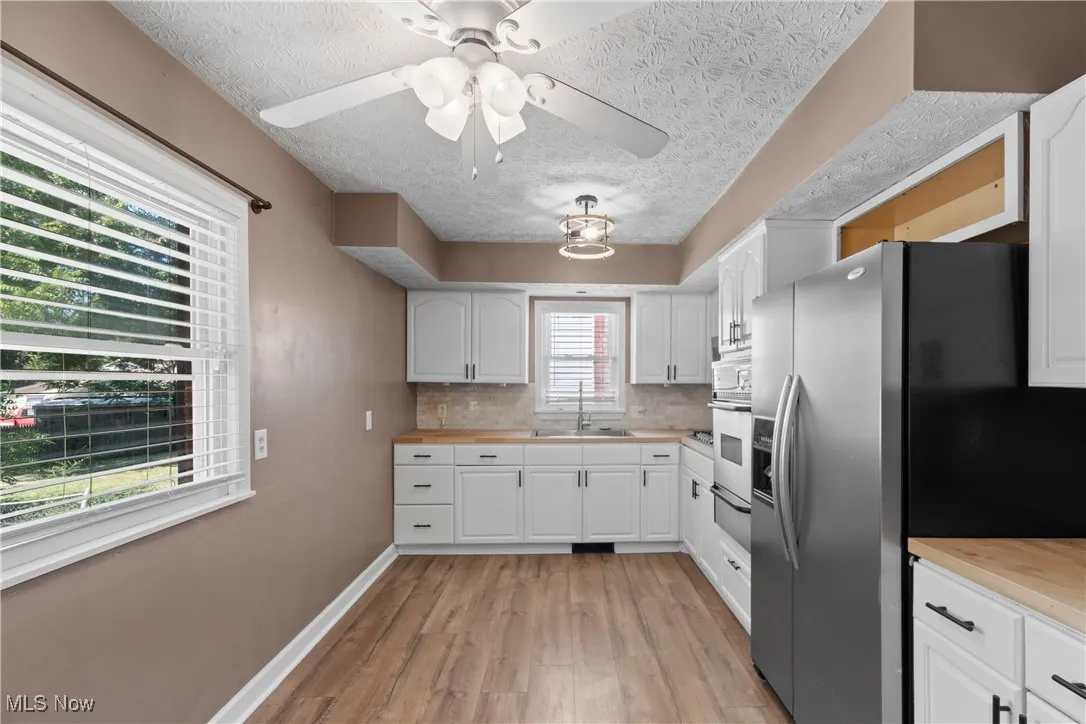 Kitchen with butcher block countertops, white cabinets, light wood-style floors, a textured ceiling, and backsplash