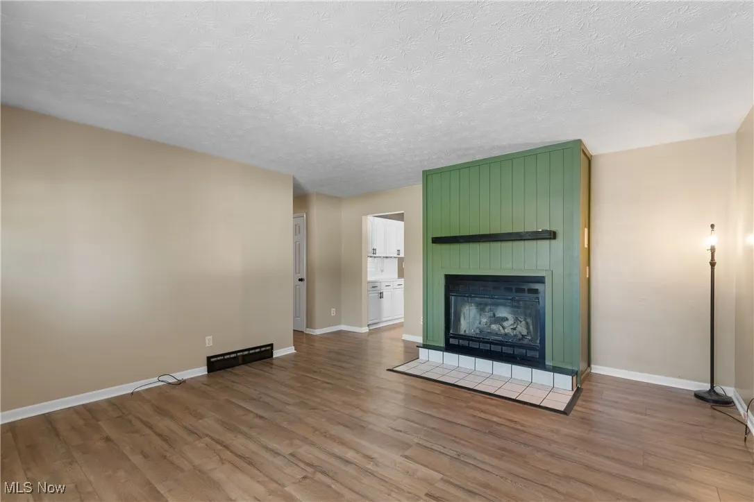 Unfurnished living room featuring a tiled fireplace, wood finished floors, and a textured ceiling
