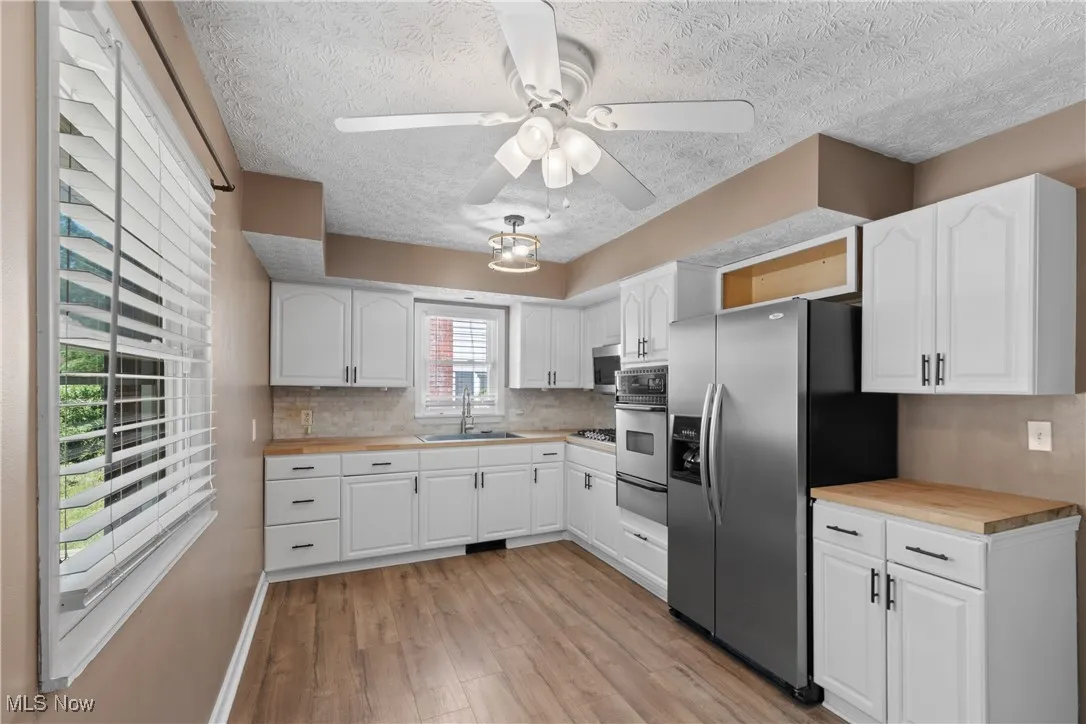 Kitchen featuring butcher block counters, stainless steel appliances, light wood-style floors, white cabinetry, and a textured ceiling