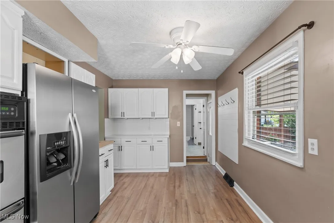 Kitchen featuring white cabinetry, stainless steel appliances, backsplash, light wood-style flooring, and a textured ceiling