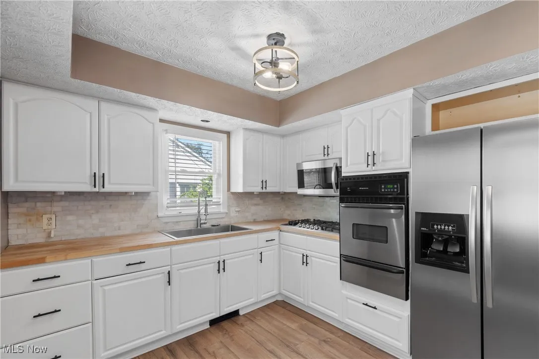 Kitchen featuring stainless steel appliances, a textured ceiling, light wood-type flooring, white cabinetry, and decorative backsplash