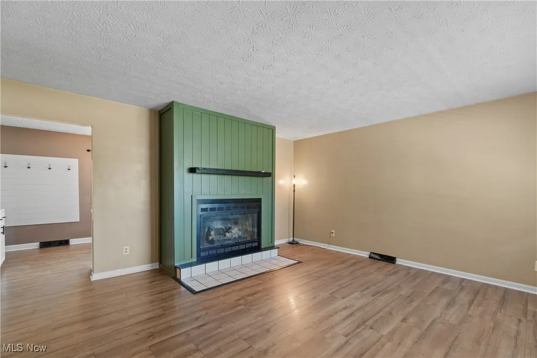 Unfurnished living room with light wood-style flooring, a tiled fireplace, and a textured ceiling