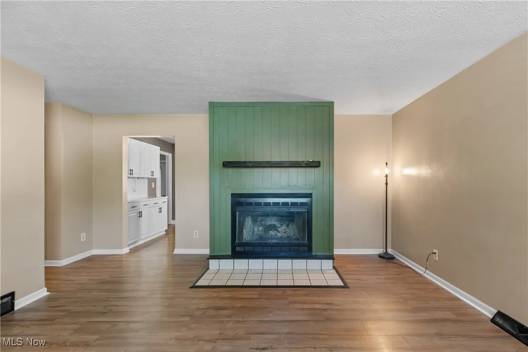 Unfurnished living room with a large fireplace, wood finished floors, and a textured ceiling
