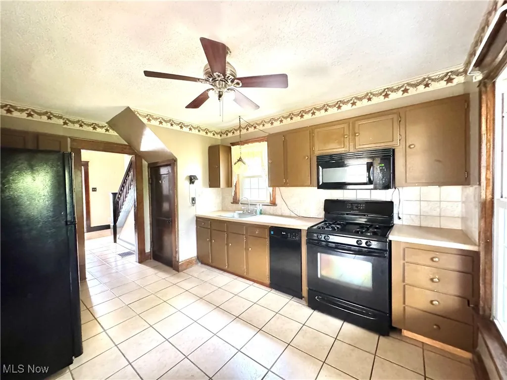 Kitchen with black appliances, tasteful backsplash, a textured ceiling, light countertops, and light tile patterned flooring