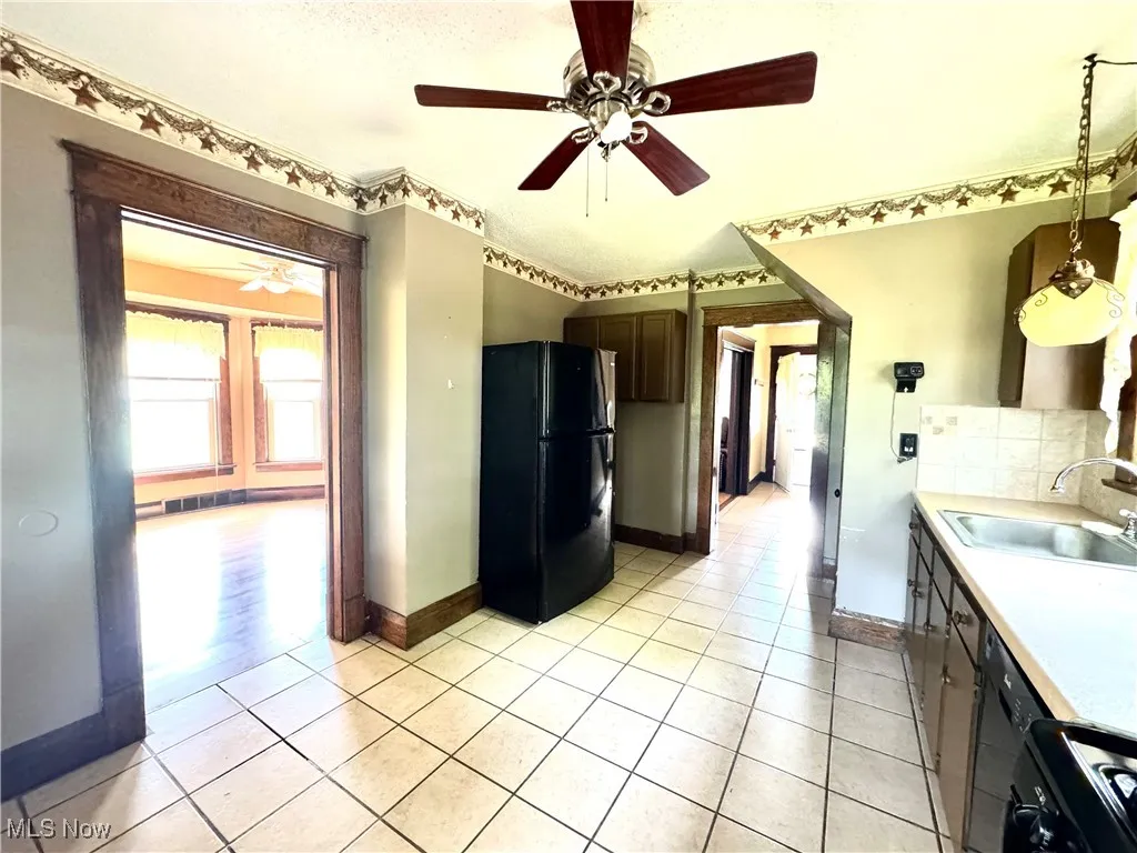 Kitchen with black appliances, light countertops, light tile patterned flooring, and decorative backsplash