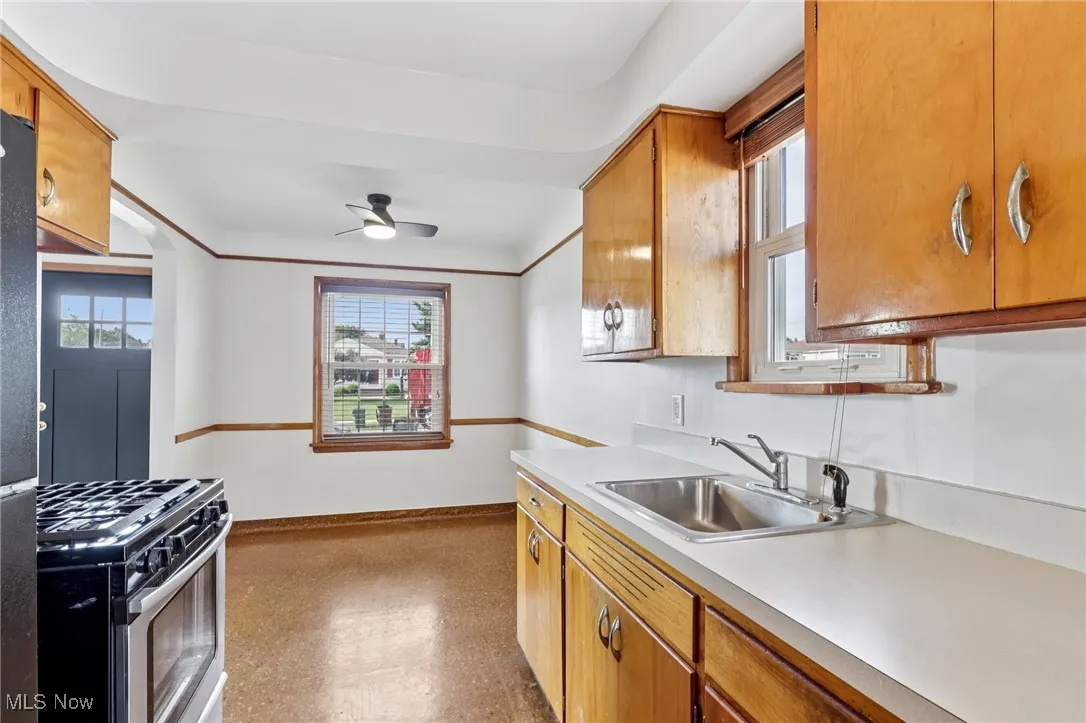 Kitchen featuring gas range, light countertops, brown cabinets, ceiling fan, and light floors