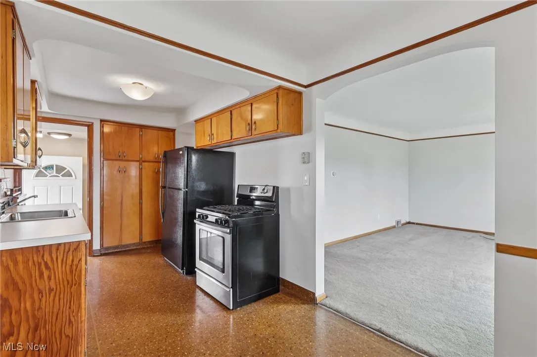 Kitchen featuring brown cabinets, stainless steel gas stove, light countertops, and arched walkways