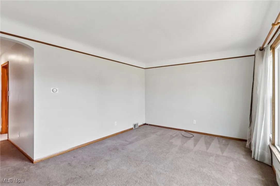 Unfurnished room featuring arched walkways and light colored carpet