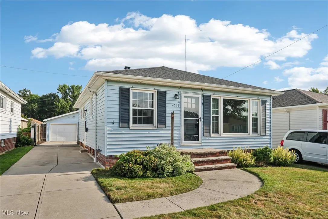 View of front of home with a detached garage, an outdoor structure, a front yard, and roof with shingles