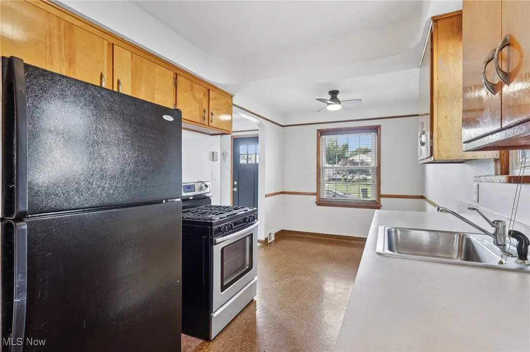 Kitchen with freestanding refrigerator, stainless steel gas range, light countertops, ceiling fan, and brown cabinetry