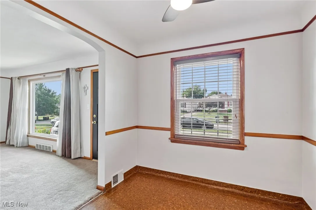 Empty room with arched walkways, plenty of natural light, carpet flooring, and a ceiling fan