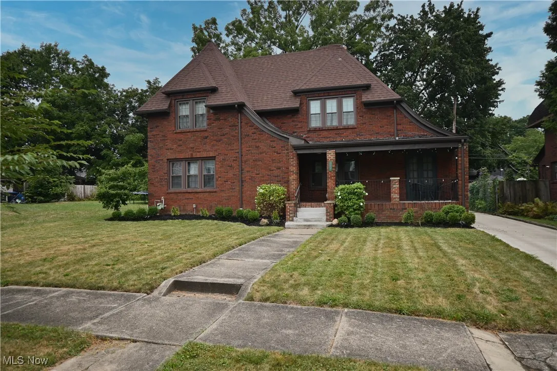 View of front of house featuring a front lawn, covered porch, brick siding, and chimney