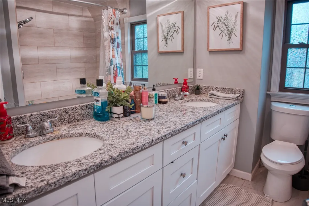 Bathroom with double vanity, tiled shower, and light tile patterned floors