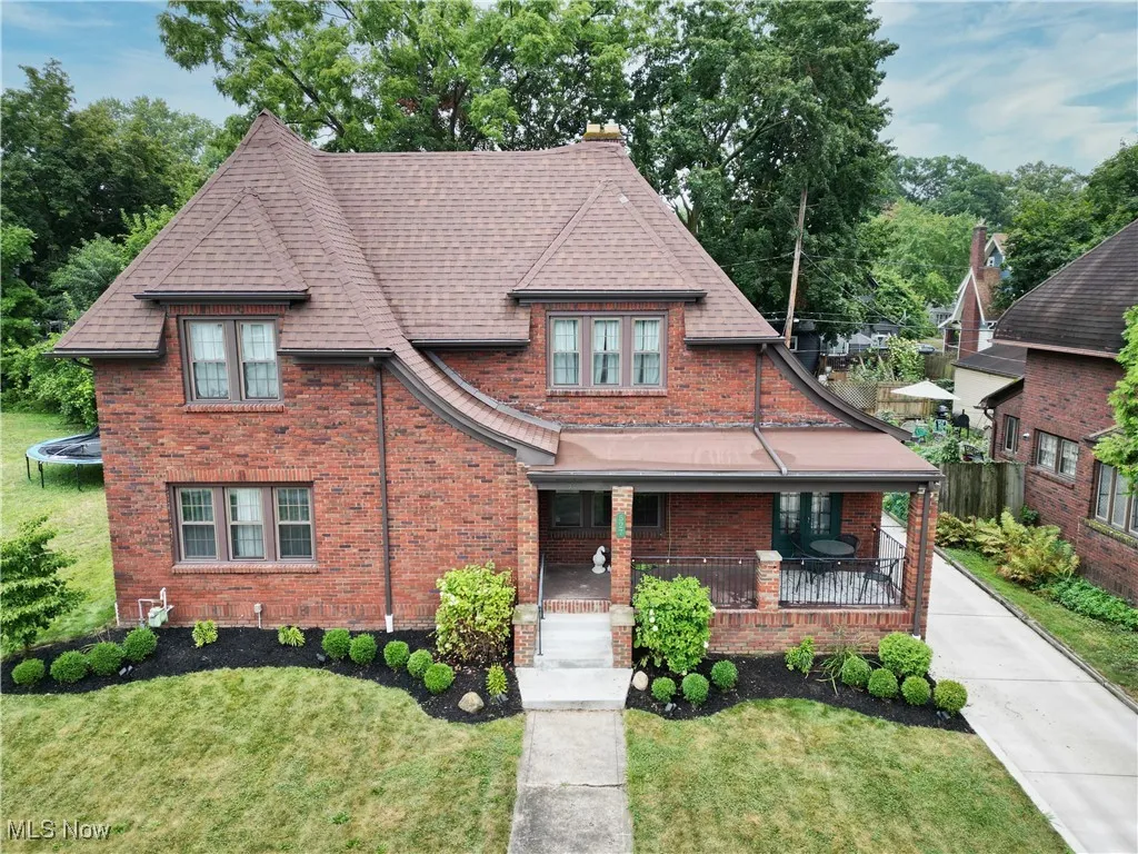 View of front of house featuring a front lawn, covered porch, brick siding, and chimney