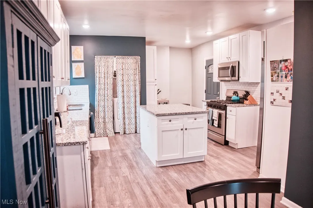 Kitchen with tasteful backsplash, white cabinetry, appliances with stainless steel finishes, light LVT flooring, and a center island