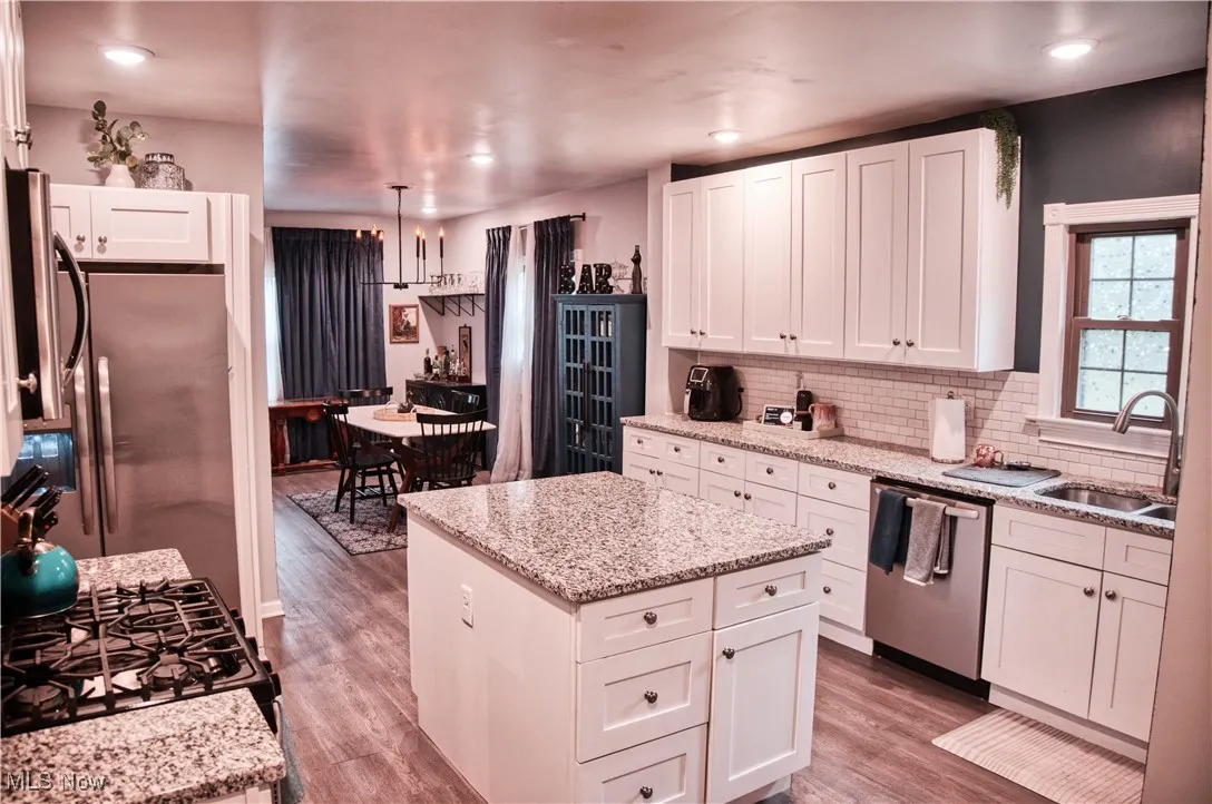 Kitchen featuring white cabinetry, light LVT floors, appliances with stainless steel finishes, light stone countertops, and decorative backsplash